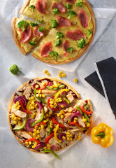 Pizzen auf betonaehnlichem Fond mit Mais Paprika Haehnchenstreifen und Schinken als Topshot, Pizza, Gemüse, 