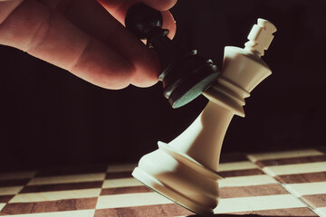 Black pawn knocking down white king on chessboard © Juanmi