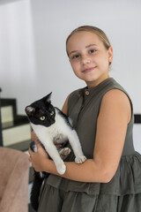 Attractive young girl hugging her cat pet sitting on cosy sofa, relaxing at home. Child and domestic kitten indoor.