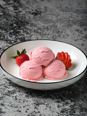 A delightful bowl of three pink strawberry ice cream scoops, artfully arranged with fresh strawberries