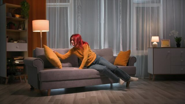 A beautiful red head woman in her casual clothers lyes to the sofa, then quickly stand up, adjust the pillow and run away. Long shot. Slow motoin