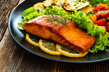 Seared salmon steak with cherry tomato salad and fried potato slices on wooden table	