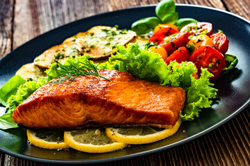 Seared salmon steak with cherry tomato salad and fried potato slices on wooden table	