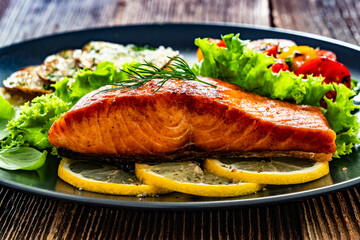 Seared salmon steak with cherry tomato salad and fried potato slices on wooden table	