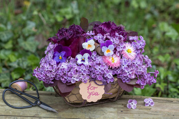 Blumen-Arrangement mit lila Hornveilchen (Viola cornuta), Gänseblümchen (Bellis perennis), Tulpen und Fliederblüten (Syringa) im Korb	
