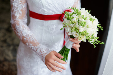 Close-Up of Bride Holding Bouquet in Elegant White Lace Wedding Dress..