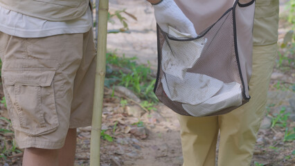Close-up of a person wearing a glove placing trash into a reusable bag while hiking in a forest, promoting eco-conscious habits, green living, sustainable trekking, and nature protection.
