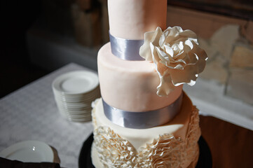 A beautifully designed three-tiered wedding cake featuring a floral decoration and elegant silver...