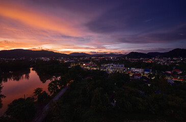 A vibrant cityscape captured at twilight, showcasing beautifully illuminated streets, serene reflective water, and a breathtaking sunset sky over a mountainous backdrop.