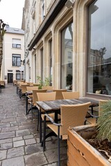 Empty restaurant summer terrace with tables and chairs. Green cafe terrace on the pedestrian street. Reastaurant tables waiting for customers at an outdoor terrace.