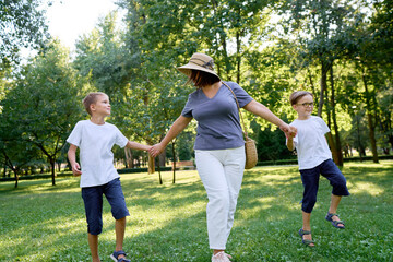 Obraz premium Mother Walking in Park With Two Sons Enjoying a Bright Sunny Day..