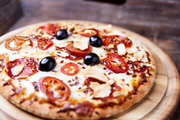 Pizza with salami and mozzarella cheese, jalapeno pepper and black olives. Wooden background. Soft focus. Close up.	