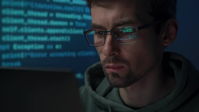 Young data scientist working late at night, computer screen lighting up his face as programming scripts scroll behind him. 