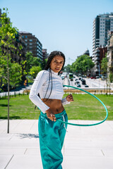 Young woman holding hula hoop in urban park, promoting healthy lifestyle and fitness