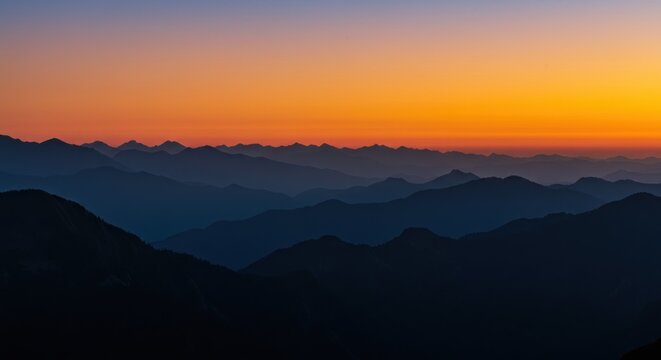 The sunrise over the mountains glows orange, casting warm light across the peaks and creating a breathtaking morning landscape.

