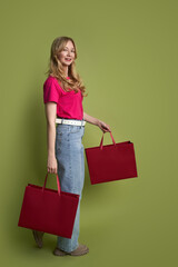 Stylish woman with red shopping bags against green background