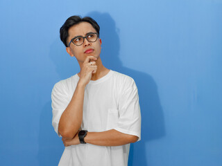 A young Asian man in a white t-shirt appears deep in thought, looking doubtful and confused about...