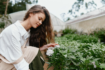 Beautiful young woman appreciating flowers in a green garden, showcasing a serene emotion and...