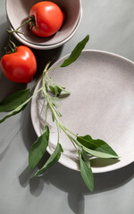 Flat lay of gray monochrome plates with tomatoes and sage. Culinary concept with space for text
