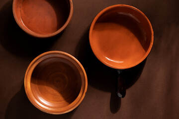 Arrangement of ceramic plates on brown background. Earthenware pottery objects, space for text. 
