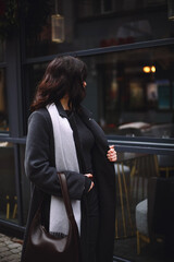 Back view of stylish brunette woman in gray coat and scarf walking on the street in winter. Beauty and fashion