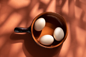 Handmade ceramic plates with home eggs on brown background. Terracotta objects, space for text. Genuine food concept.

