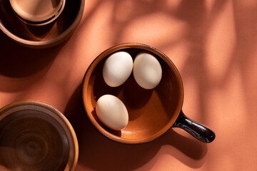 Handmade ceramic plates with home eggs on brown background. Terracotta objects, space for text. Genuine food concept.
