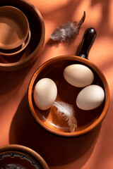 Handmade ceramic plates with home eggs on brown background. Terracotta objects, space for text. Genuine food concept.
