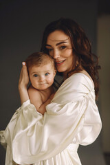Happy  mother in designer dress holding her baby girl while posing on black background