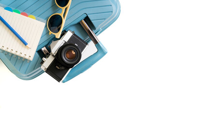 A blue suitcase with a camera, sunglasses and a notebook on top of it. The notebook is on the left side of the suitcase. The camera is a vintage model. white copy space