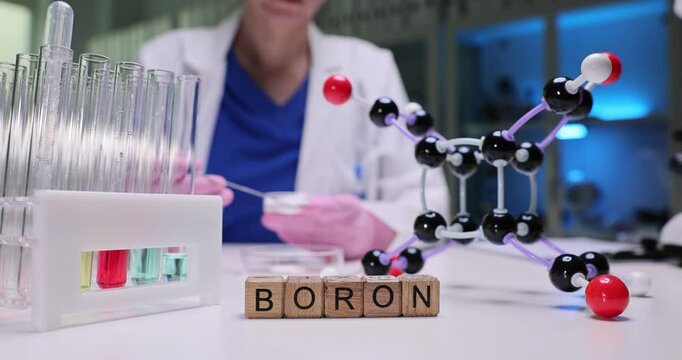 A scientist demonstrates a boron experiment with a molecular model and test tubes in a lab for education
