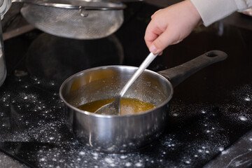 Child stirring melted ingredients in a saucepan on the stove