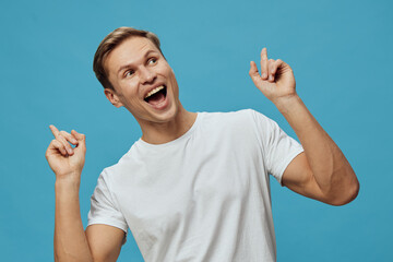 Bright cheerful young man with short brown hair smiling widely and pointing upward with both hands,...