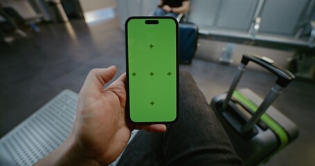 Crowded Airport Terminal: POV Man Sitting in Departure Lounge, Scrolling Smartphone with Green...
