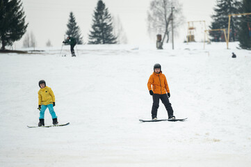Two young snowboarders carving through fresh snow at a charming winter resort on a crisp day filled...