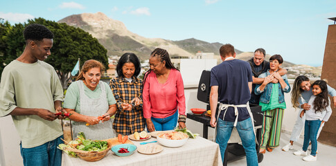 Multigenerational people doing barbecue at home's rooftop - Multiracial friends having fun cooking together during weekend day - Summer and food concept - Main focus on left latin woman face