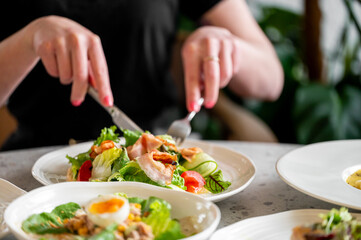 A close-up of hands using a knife and fork to eat a fresh salad with lettuce, tomatoes, and a boiled egg. The image highlights healthy eating and fresh ingredients