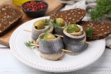 Delicious herring rolls with olives, dill and bread on white wooden table, closeup