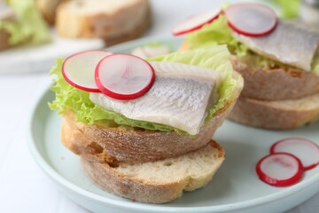 Tasty sandwiches with herring, radish and lettuce on table, closeup