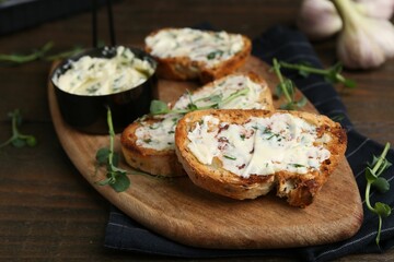Tasty bread with garlic, herbs and oil on wooden table, closeup