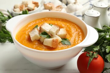 Tasty pumpkin cream soup with croutons, parsley and tomato on white marble table, closeup
