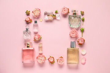 Frame of bottles with perfume and beautiful flowers on pink background, flat lay. Space for text