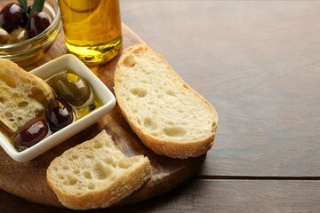 Slices of bread with oil and olives on wooden table, closeup. Space for text