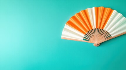 A beautifully designed fan in orange and white, elegantly placed on a serene aqua background, reflecting the beauty of simplicity and the art of decorative objects.