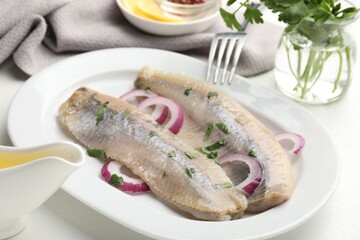 Tasty herring fillets with onions and parsley served on white table, closeup