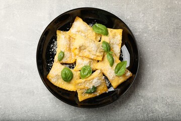 Delicious ravioli with parmesan cheese and basil on grey table, top view
