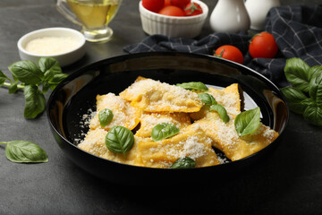 Delicious ravioli with parmesan cheese and basil on black table