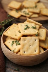 Tasty salty crackers with thyme on wooden table, closeup