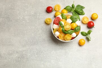 Fresh salad with yellow tomatoes, basil and mozzarella cheese on grey table, flat lay. Space for text