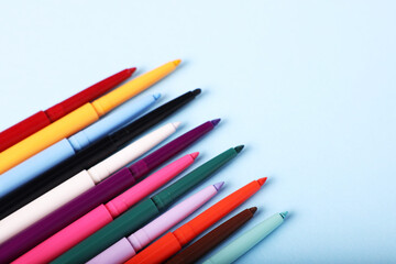 Colorful twist up eye pencils on light blue background. Space for text